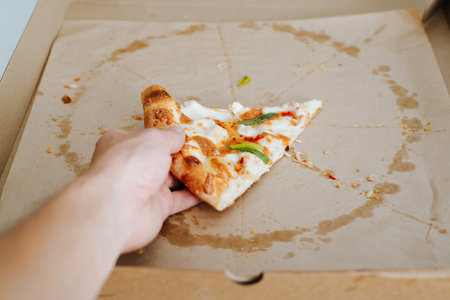 Eaten pizza. Close-up of a hand taking the last one slice of cheesy pizza from a cardboard box.の写真素材