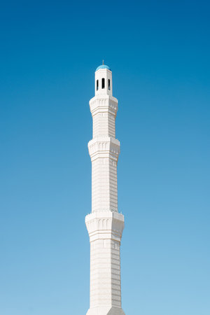 White tower of the minaret of the mosque for the call to prayer against the backdrop of a clear blue...