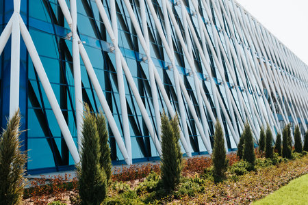 Side view of a metal geometric structure of a building with glass blue windows. Close-up exterior wall of a modern building with steel pipes and decorative trees.の写真素材