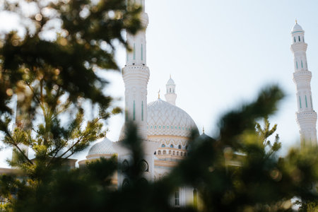 Part of white mosque, beautiful Muslim prayer building with minarets on clear sunny day outdoors, looking through trees.の写真素材