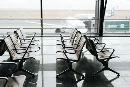 Empty waiting room at international airport. Side view of row of seating chairs against background of window with an airplane, selective focus.の写真素材