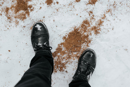 Person in black leather winter boots standing on snow, close-up.の写真素材