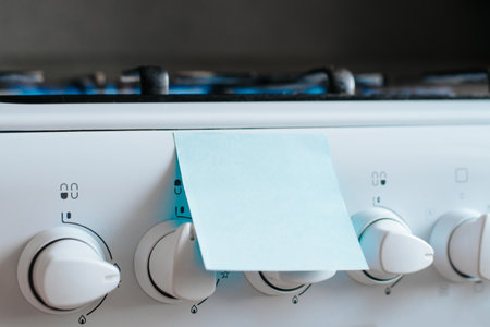 Mock up reminder sticker with blank space pasted on gas stove panel in kitchen, selective focus.