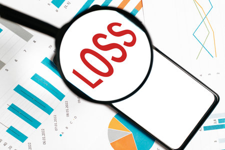 Magnifier focused on Loss word on smartphone screen, business financial documents with charts and infographics on desktop, top view. Investment banking crisis concept.の写真素材