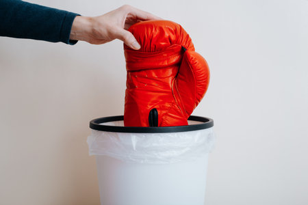 Close-up of hand throwing red boxer glove into trash can, indoors. Refusal from sports concept.の写真素材