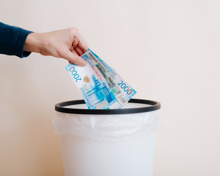 Close-up of hand throwing money rubles into trash can, indoors.の写真素材