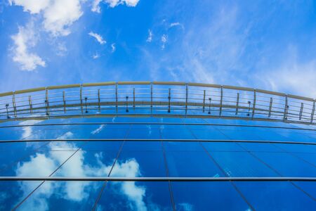 Modern blue glass business building reflecting sky with clouds
