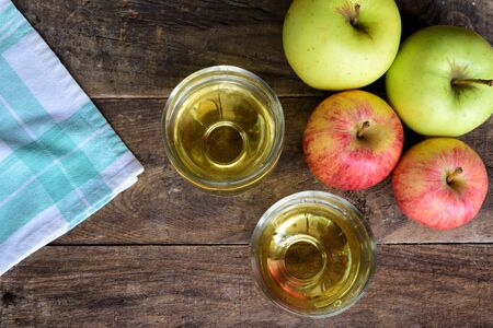 A bunch of apples with two glasses with apple juice on top of a old wood table and a green and white table clothの写真素材