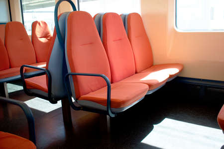 Inside of a train cabin with orange seats and sunlight coming in through the windowsの写真素材