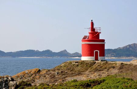 Red and white lighthouse on the coast of La Vela in Cangas do Morrazo with the Atlantic Ocean and the islands Cies in the backgroundのeditorial素材