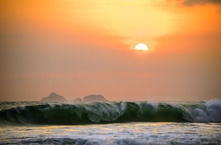 Incredible beautiful orange sunset with mountains in the background and big waves of Atlantic ocean at Ipanema beach in Rio de Janeiro, Brazilの写真素材