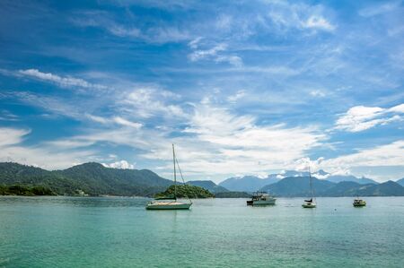 Boats floating in the turquoise water against the background of mountains and beautiful blue sky with spindrift clouds next to Ilha Grande, Angra dos Reis, RJ, Brazilの写真素材