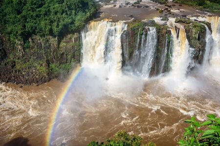 Rainbow and view of cascading water of Iguazu Falls with extensive tropical forest and raging river in Iguacu National Park,   Foz de Iguacu, Parana State, Brazilの写真素材