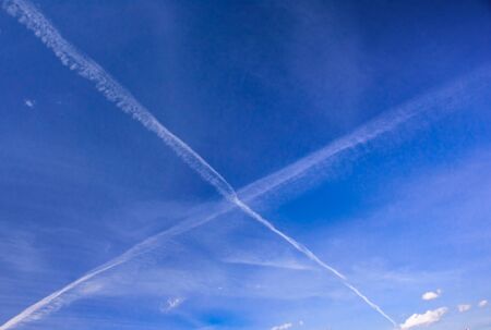 Blue spring sky with X-shaped traces of aircrafts at sunny dayの写真素材