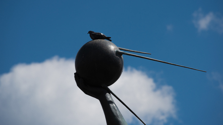 Closeup of hand holding the first artificial earth satellite with dove sitting on it and blue sky with white cloud on the backgroundの写真素材