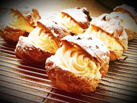 Eclairs with cream on a cooling rack. Toned.