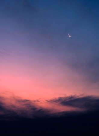 the moon rises at sunset in a sky with low clouds