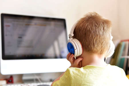 blond boy sitting in front of a computer studying with headphones from homeの写真素材