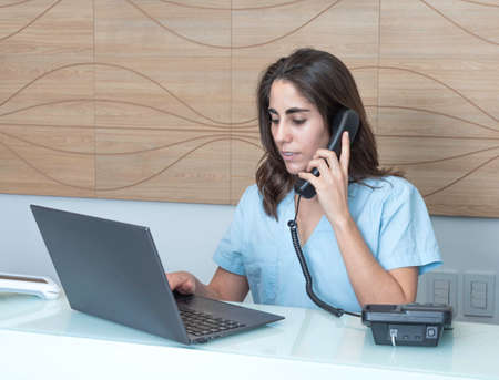 young woman working at the reception of a dental office, talking on the phone and smilingの写真素材