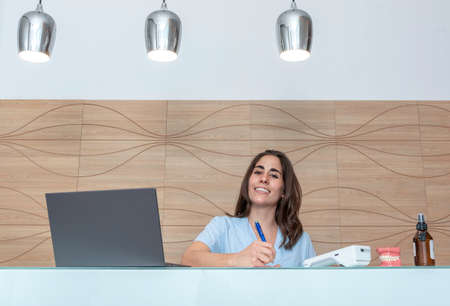 young woman working at the reception of a dental office, talking on the phone and smilingの写真素材