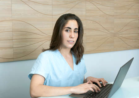 young woman working at the reception of a dental office, talking on the phone and smilingの写真素材