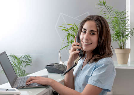 young woman working at the reception of a dental office, talking on the phone and smilingの写真素材