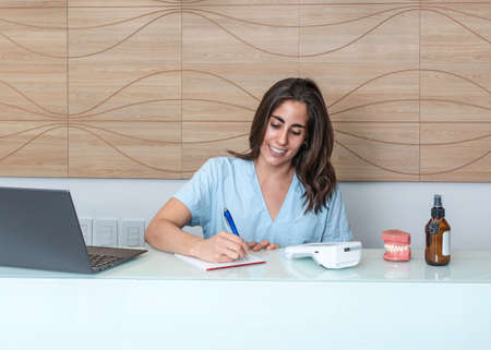 young woman working at the reception of a dental office, talking on the phone and smilingの写真素材