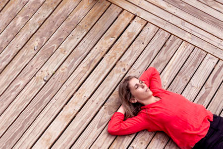 woman sunbathing on a wooden dec with her arms crossed behind her headの写真素材