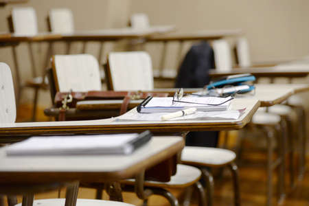 desks in a classroom with notebooks and pens, with no people occupying the seats.の写真素材