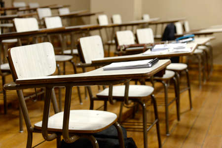 desks in a classroom with notebooks and pens, with no people occupying the seats.の写真素材
