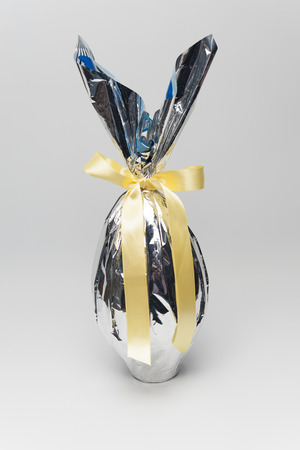 Homemade Easter egg in beautiful silver packaging with yellow ribbon. Isolated on white background. Vertical image. Close-up.の写真素材