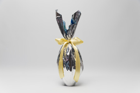 Homemade Easter egg in beautiful silver packaging with yellow ribbon. Isolated on white background. Horizontal image with space for text.の写真素材