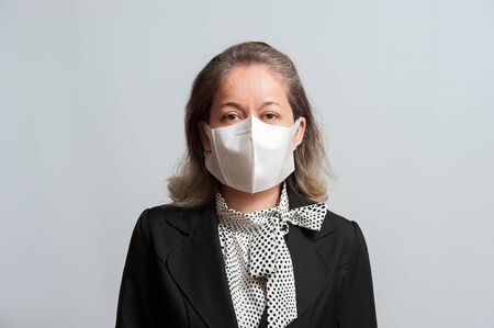 Front view of middle aged mixed race woman in formal wear wearing white surgical mask for protection against coronavirus (COVID-19) and other infectious diseases. Isolated on white background. Horizontal shot.の写真素材