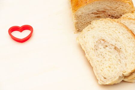 Brazilian homemade bread sliced next to a red heart shape object. Isolated on light wooden...