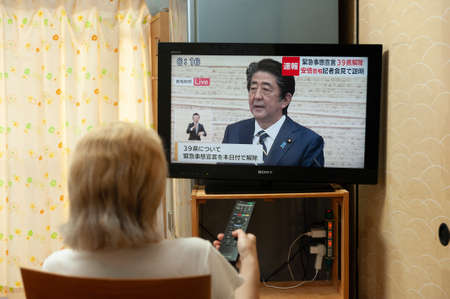 Fuji City, Shizuoka, Japan - May 14, 2020: Coronavirus (COVID-19) Pandemic. A woman watches on Japanese TV [LIVE] Interview by PM Shinzo Abe about cancelingのeditorial素材