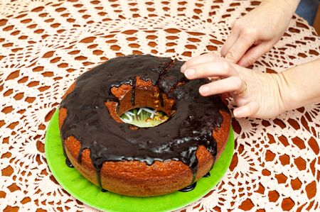 Hands slicing delicious and healthy traditional Brazilian homemade carrot cake with chocolate sauce. Top view. Copy space. Background with crochet towel.の写真素材
