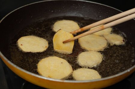 Brazilian cuisine - Frying homemade sweet potatoes in cooking oil handled with chopsticks. Close-up. Horizontal shot.の写真素材