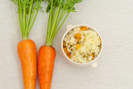 Vegetarian / vegan cuisine - Raw carrots with leaves and a bowl of cooked rice with carrots. Isolated on white background. Copy space. Top view. Horizontal shot.の写真素材