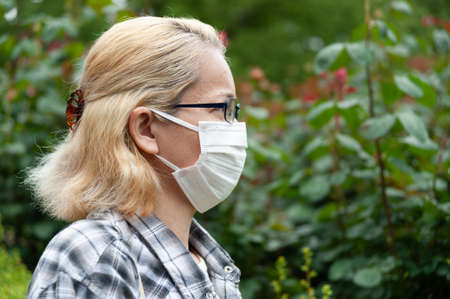 Side view portrait of middle aged mixed race blonde woman with eyeglasses wearing white surgical mask. Protection against coronavirus (COVID-19) and other infectious diseases. Billboards. Copy space.の写真素材