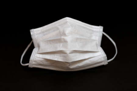 White surgical mask for protection against coronavirus (COVID-19) and other infectious diseases. Close-up. Horizontal shot. Isolated on black background.の写真素材