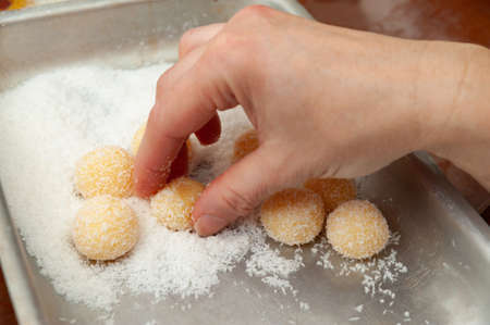 Woman hand making Beijinho de Coco, a traditional Brazilian candy called Coconuts Little Kiss. Side...
