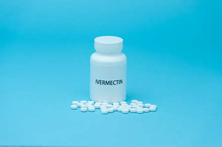 Treatments for Coronavirus (COVID-19): IVERMECTIN in white bottle packaging with scattered pills. Isolated on blue background.の写真素材