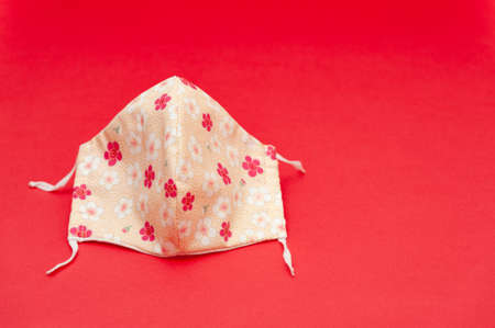 Floral pattern (red, white and salmon color) DIY fabric face mask for protection against coronavirus (COVID-19) and other infectious diseases. Isolated on red background. Copy space. Horizontal shot.の写真素材