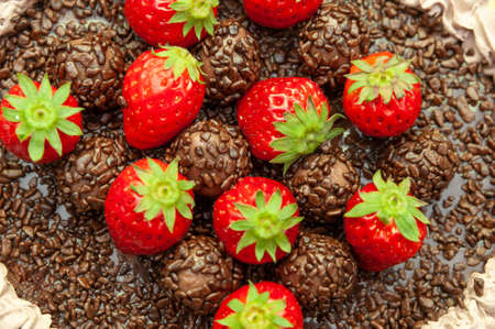 Homemade chocolate cake covered with chocolate sprinkles and fresh strawberries. Known in Brazil as "Brigadeiro Cake". Isolated on yellow background. Top view. Close-up.の写真素材