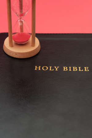 Holy Bible, the Word of God with hourglass. Isolated on red background. Top view. Close-up. Vertical shot.の写真素材