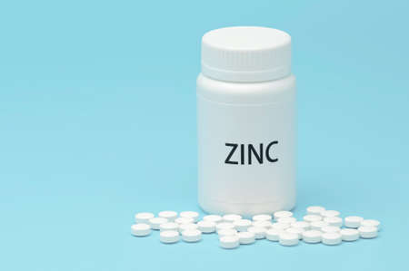 ZINC in white bottle packaging with scattered pills. Nutritional supplement. Treatments for COVID-19. isolated on blue background. Horizontal shot. Copy space.の写真素材