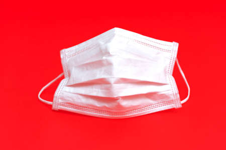 White surgical mask for protection against Coronavirus (COVID-19) and other infectious diseases. Close-up. Horizontal shot. Isolated on red background.の写真素材