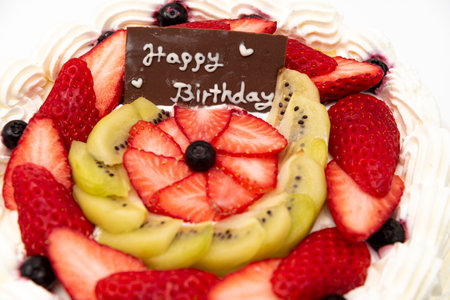 Homemade birthday cake decorated with strawberries, kiwi fruit and blueberries isolated on white background in side view and closeup.の写真素材