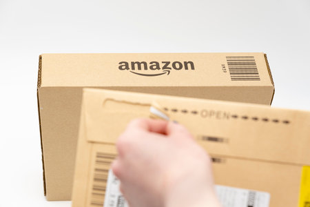 Fuji City, Shizuoka-Ken, Japan - March 26, 2023: Hand opening delivery envelope with selective focus on Amazon logo on cardboard box in background. Isolated on white background with copy space.のeditorial素材