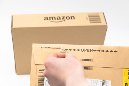 Fuji City, Shizuoka-Ken, Japan - March 26, 2023: Hand opening delivery envelope with cardboard box with Amazon logo slightly blurred in background. Isolated on white background.のeditorial素材